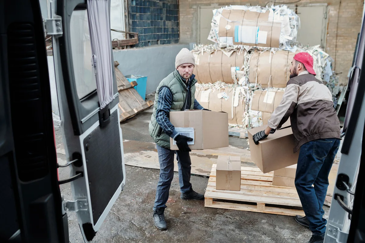 Workers moving cardboard boxes beside a delivery van